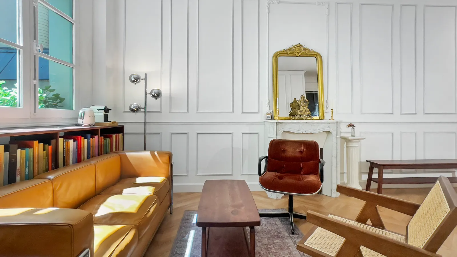 Salon haussmannien avec cheminée en marbre, miroir doré et canapé en cuir cognac